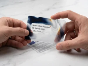 Hand holding a frosted glass card over personal data on marble, selectively obscuring sensitive information beneath an EU regulatory document.