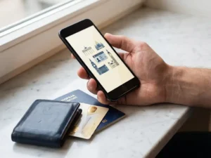 Hand holding a smartphone above a leather wallet, passport, and health card fanned on marble, illustrating European digital ID consolidation.